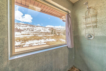 Shower room with large window with snowy grassy landscape and blue sky views
