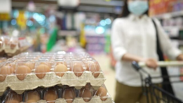 close up woman wear protective face mask buying egg in to shopping cart in supermarket