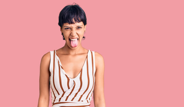 Young brunette woman with short hair wearing summer outfit sticking tongue out happy with funny expression. emotion concept.