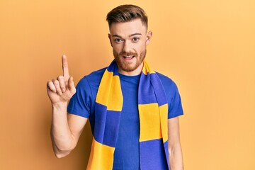 Young redhead man football hooligan cheering game smiling with an idea or question pointing finger up with happy face, number one