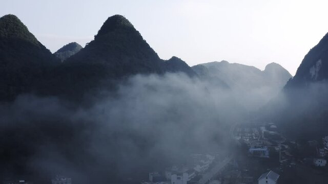 Asian karst mountains at sunset rising above remote town below clouds, aerial