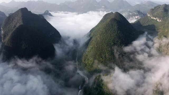 Asian karst mountains rising above clouds and small Chinese town, aerial