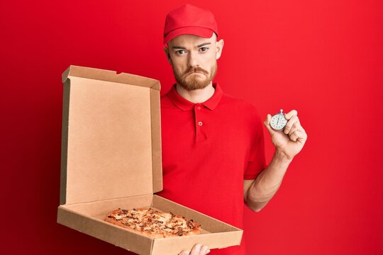 Young Redhead Man Wearing Delivery Uniform Holding Pizza Box And Countdown Clock Depressed And Worry For Distress, Crying Angry And Afraid. Sad Expression.