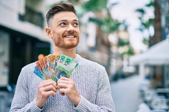 Young caucasian man smiling happy holding australian dollars at the city.