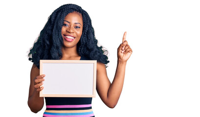 Beautiful african american woman holding blank empty banner surprised with an idea or question pointing finger with happy face, number one