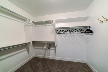 Empty walk in closet of home with white wall and hanges hanging on netal rods