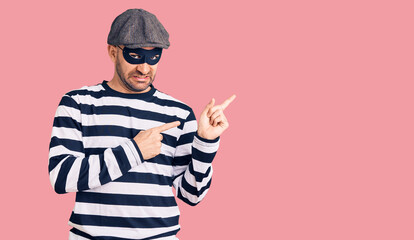 Young handsome man wearing burglar mask pointing aside worried and nervous with both hands, concerned and surprised expression