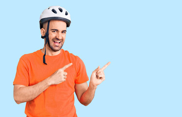 Young handsome man wearing bike helmet smiling and looking at the camera pointing with two hands and fingers to the side.