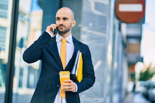 Young hispanic bald businessman with serious expression talking on the smartphone drinking coffee at the city