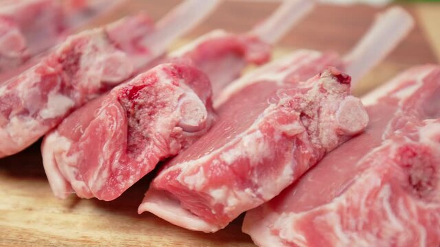 Close-up raw chopped lamb ribs on cutting board with decorative vegetables in 4K. Concept of fresh redraw lamb cutlets sliced from a rack with bones nicely arranged on the table in slow-motion.
