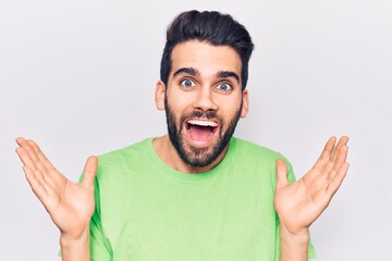 Young handsome man with beard wearing casual t-shirt celebrating victory with happy smile and winner expression with raised hands