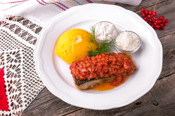 Mamaliga with butter and fish cooked on a grill in tomato sauce with sour cream and salted cheese. Balkan cuisine. National cuisine. Nourishing, useful, natural. Rustic cuisine.