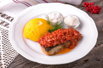 Mamaliga with butter and fish cooked on a grill in tomato sauce with sour cream and salted cheese. Balkan cuisine. National cuisine. Nourishing, useful, natural. Rustic cuisine.