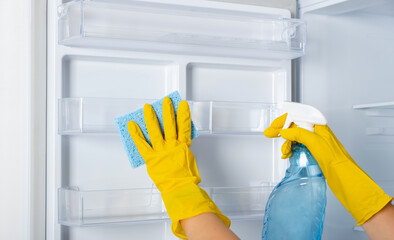 A woman's hands in a yellow rubber protective glove and a blue sponge washes, cleans refrigerator...
