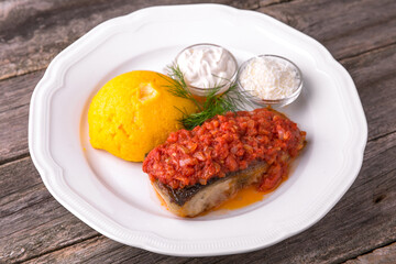 Mamaliga with butter and fish cooked on a grill in tomato sauce with sour cream and salted cheese. Balkan cuisine. National cuisine. Nourishing, useful, natural. Rustic cuisine.