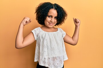 Young little girl with afro hair wearing casual clothes showing arms muscles smiling proud. fitness concept.