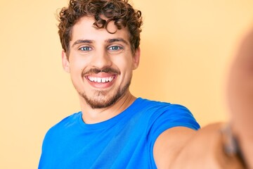 Fototapeta na wymiar Young caucasian man with curly hair wearing casual clothes taking a selfie looking positive and happy standing and smiling with a confident smile showing teeth