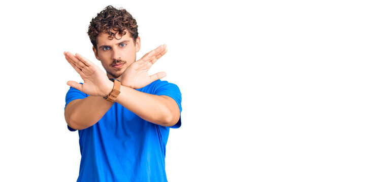Young handsome man with curly hair wearing casual clothes rejection expression crossing arms and palms doing negative sign, angry face