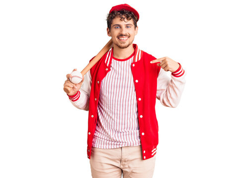 Young handsome man with curly hair playing baseball holding bat and ball pointing finger to one self smiling happy and proud