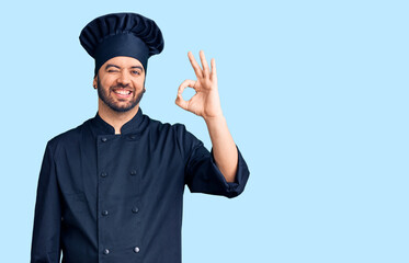 Young hispanic man wearing cooker uniform smiling positive doing ok sign with hand and fingers. successful expression.