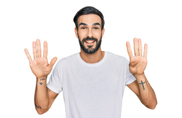 Young hispanic man wearing casual white t shirt showing and pointing up with fingers number nine...
