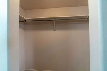 Walk in closet of home with built in wooden wall shelf above metal clothes rods