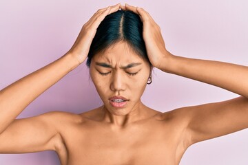 Young chinese woman standing topless showing skin suffering from headache desperate and stressed because pain and migraine. hands on head.