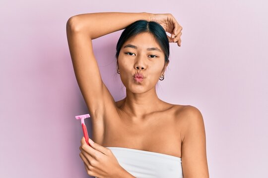 Young chinese woman wearing shower towel using razor looking at the camera blowing a kiss being lovely and sexy. love expression.