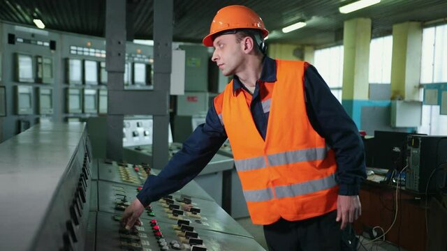 Worker pressing buttons on CNC machine control board in factory. Young engineer technician pressing one control panel industrial machine. lit lights, dials on manufacturing machinery by controller