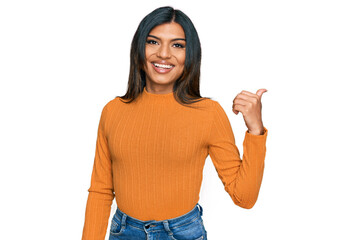 Young latin transsexual transgender woman wearing casual clothes smiling with happy face looking and pointing to the side with thumb up.