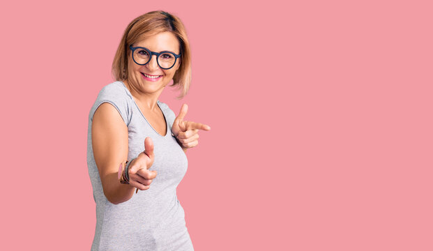 Young blonde woman wearing casual clothes pointing fingers to camera with happy and funny face. good energy and vibes.