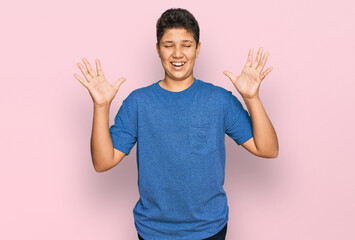 Teenager hispanic boy wearing casual clothes celebrating mad and crazy for success with arms raised...
