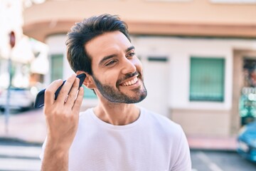 Young hispanic man smiling happy listening audio message using smartphone at city.