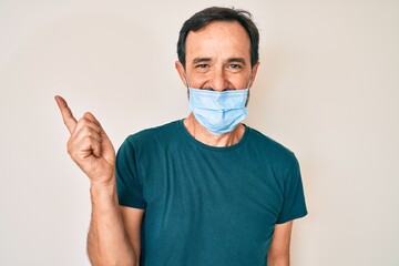 Middle age hispanic man wearing medical mask smiling happy pointing with hand and finger to the side