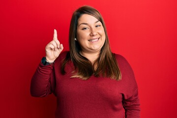 Beautiful brunette plus size woman wearing casual clothes pointing finger up with successful idea. exited and happy. number one.