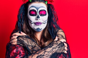 Young woman wearing day of the dead costume over red hugging oneself happy and positive, smiling confident. self love and self care