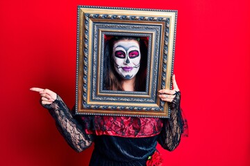 Obraz premium Young woman wearing day of the dead costume holding empty frame smiling happy pointing with hand and finger to the side