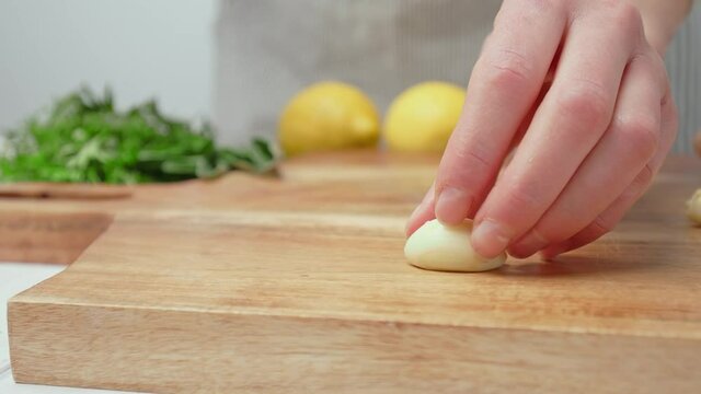 Chef crushing garlic close-up and squeeze with a side knife in 4K. Concept of a woman chef squeezing a bunch of garlic with hand on a cutting board in slow-motion.