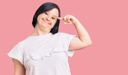 Brunette woman with down syndrome wearing casual white tshirt smiling pointing to head with one...