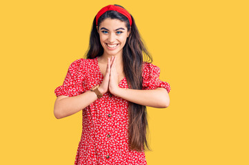 Brunette teenager girl wearing summer dress praying with hands together asking for forgiveness smiling confident.