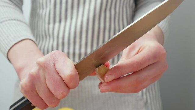 Chef peeling a fresh big garlic clove close-up in 4K. A woman chef cleaning the garlic with a knife on macro background in slow-motion.