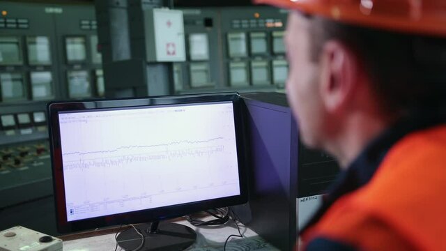 Male uses computer showing system monitoring, controlling program. In background technology development laboratory with scientists, working. Industrial engineer. Work at heavy industry manufacturing