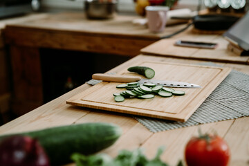 Organic vegetables assortment on kitchen wooden counter table with cutting board and knife. vegetarian recipe healthy meal lifestyle concept. closeup on chopped cucumber slices on wood cooking place