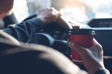 Man holding cup of coffee while driving a car in the morning