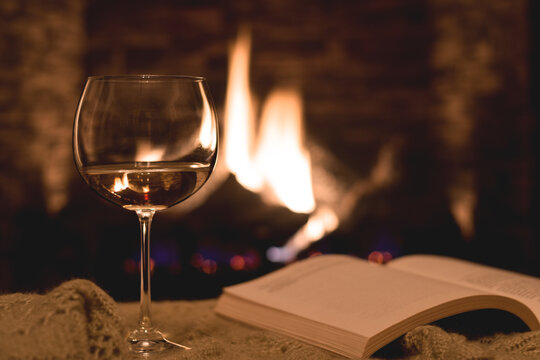 A glass of white wine and an open book in front of fireplace