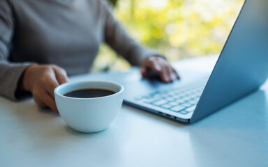 Closeup image of a woman working and touching on laptop computer touchpad while drinking coffee