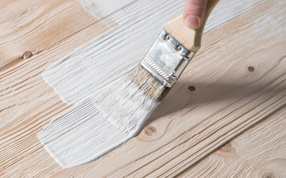 Painted wooden surface with brush and white paint. Natural wooden texture. Renovation or repair construction. 