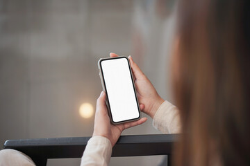 Backside view of woman hand using mockup white screen mobile phone.