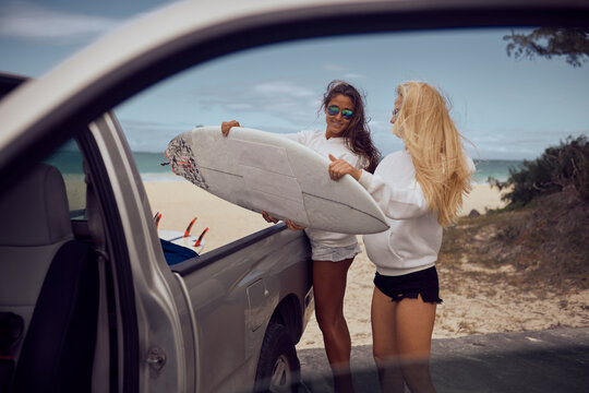 Two Young Women Taking Out Surf Boards From Car Trunk