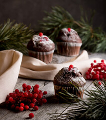 Delicious cupcakes decorated with red berries on a wooden background with spruce branches. Sweets for the celebration of Christmas. Holiday concept.